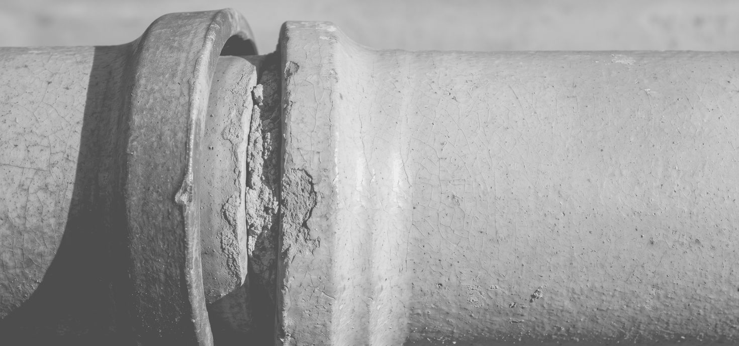 Macro photograph of a fired clay conduit: a spigot-and-socket joint where one pipe is seated into the collar of the next, the seam packed and the glaze crazed with age.